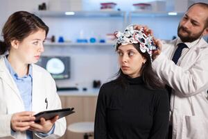 Professional neurological researcher explaning treatment result pointing on monitor while medical scientist adjusting eeg headset, preparing for brain scan analysing electrical activity, nervous system. photo