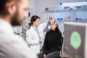 Neurologist physician in medicine lab adjusting headset with sensors, modern facility for science. Patient with brain scan, high tech tomography information. photo