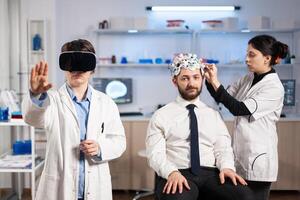 Neuroscientist wearing virtual reality headset looking at patient brain activity, wearing high tech sensors for scanning. Doctor searching diagnosis, experiment , eeg , medicine lab. photo