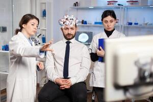 Neurological researchers explaning treatment result pointing on monitor while medical scientist adjutaking notes, scanning headset preparing for brain scan analysing electrical activity. photo