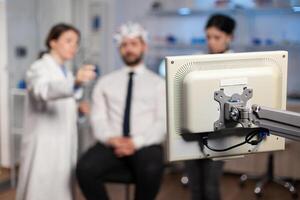 Scientist in brain study discussing with patient attached wot electrod sensors, nervous system evolution. Medical team in clinic using scanner, tomography. photo
