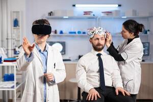 Neurologist doctor gesturing wearing virtual reality headset and assistant adjusting patient sensor that read brain activity , nervous system. Neuroscientist analysing diagnosis. photo