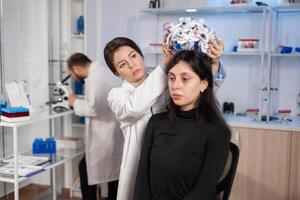 Medical lab technician putting eeg headset monitoring brain functions, descovering diagnosis of disease. Team of scientists researchers working late night in neurology clinic for woman health. photo