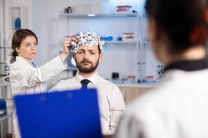 Neuroscience doctor showing on clipboard treatment against brain disease explaning to patient diagnosis of illness. Woman sitting in neurological scientific lab treating nervous system dysfunctions photo