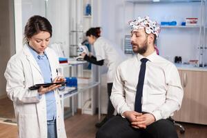 Neuroscience doctor using tablet pc treatment against brain disease explaning to patient diagnosis of illness. Woman sitting in neurological scientific lab treating nervous system dysfunctions. photo