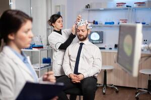 Man patient visiting professional medical researcher in neurology medicine testing brain functions with eeg headset. Doctor monitoring nervous system, descovering diagnosis of disease. photo