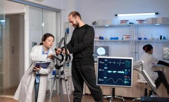 Team of medial researchers monitoring vo2 of man performance sports wearing mask running. Lab science doctor measuring endurance of sportsman while ekg scan runs on computer screen in laboratory. photo