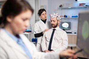 Man patient wainting for brain experiment with headset in research lab while scientist is making adjusting, inovations high tech clinic. Neurologist study nervous system. photo