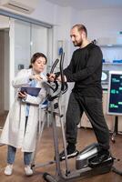 Aathlete running on cross trainer, while medical specialists supervise exercise, controlling physical activity, measuring heart rate in sports science laboratory. photo
