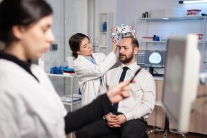 Neurology researcher adjusting brain headset on patient during study, examining nervous system. High tech technology tomography sensors , neuroscience physician. photo