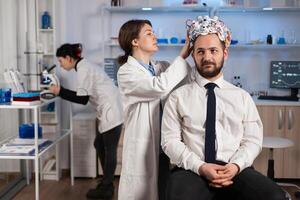 Neurologist doctor analysing brain of man and nervous system using brainwave scanning headset. Researcher using high tech developing neurological innovation monitoring side effects on monitor screen photo