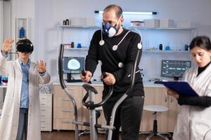 Sport performance scientist experiencing virtual reality goggles, athlete with electrodes running on cross training test. Measuring endurance with sensors. photo