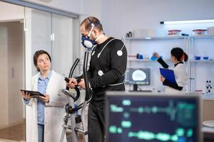Sport scientist monitoring performance of athlete cardio, heart rate, testing cross training sportman in laboratory. Healthy body ekg laboratory run. photo
