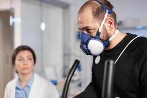 Runner athlete testing cardio heart rate in sport endurance laboratory with mask and electrodes on body, vo2. Sportman training with sensor on cross research. photo