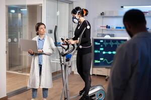 Specialist sport researcher monitoring heart rate on athlete while woman with mask running on cross trainer talking with medical doctor. Physician using laptop controling EKG data in modern laboratory. photo