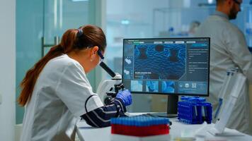 Biotechnology scientist researching in laboratory using microscope and typing on pc. Chemist examining virus evolution using high tech for scientific research of vaccine development against covid19 photo