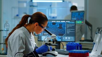 Scientist looking at biological samples under microscope typing on pc. Team of chemists working in lab, examining virus evolution using high tech for scientific research of vaccine development. photo