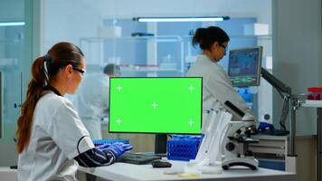 Medical research scientist working on pc with green screen mock up template in applied science laboratory. Engineers conducting experiments in background, examining vaccine evolution using high tech photo