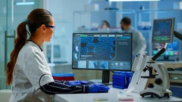 Biologist doctor checking DNA informations typing on pc in modern equipped laboratory. Scientists examining vaccine evolution in medical lab using high tech, chemistry tools for scientific research. photo