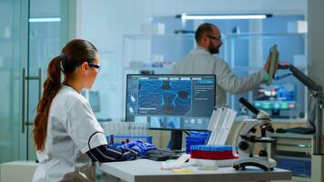 Chemistry doctor analysing blood sample and typing on computer while coworker opening door using digital computer with touch scan. Woman examining virus evolution using high tech and chemistry tools photo