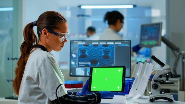 Medical research scientist working on tablet with green screen mock up template in applied science lab. Engineers conducting experiments in background, examining vaccine evolution using high tech photo