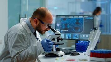 Male scientist looking under microscope in medical development laboratory, entering data in computer. Specialists working on medicine, biotechnology research in advanced pharma lab photo