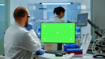 Researcher looking at chroma key display in modern equipped lab analysing virus evolution. Team of microbiologists doing vaccine research writing on device with green screen, isolated, mockup display. photo