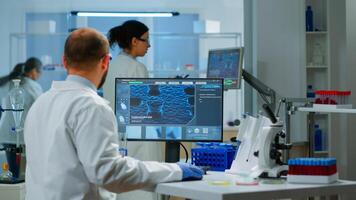 Man scientist working to develop a new vaccine in modern equipped laboratory, typing at computer. Group of biochemistry doctors examining virus evolution using high tech for researching treatment photo