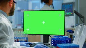 Man doctor working at pc with green screen in modern equipped lab analysing virus evolution. Team of microbiologists doing vaccine research writing on device with chroma key, isolated, mockup display. photo