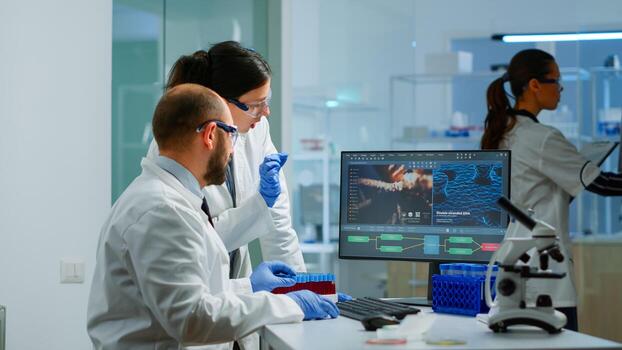 Team medical scientist conducting DNA experiments looking in computer holding test tube with blood sample working in science laboratory. Lab engineers in white coat analysing vaccine development photo