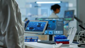 Close up of scientist in lab coat working holding tablet standing in modern equipped laboratory. Team chemists examining vaccine evolution using high tech and chemistry tools for virus development photo