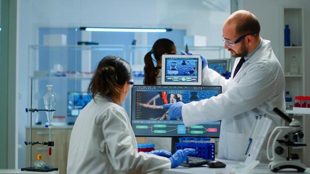 Chemists worried about virus evolution comparing DNA informations from tablet discussing in laboratory. Stuff examining vaccine development using high tech researching treatment against covid19 virus photo