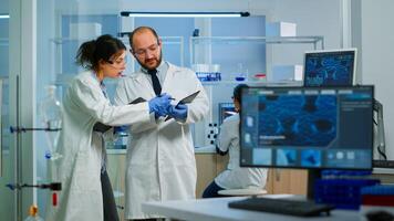 Scientists coworkers using digital tablet working in medical research laboratory, analysing biochemicals samples, talking. Scientific lab for medicine, microbiology development with advanced equipment photo