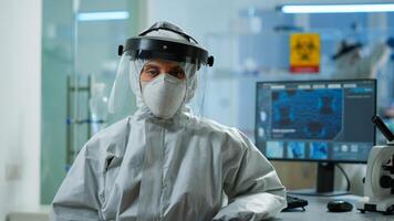 Tired microbiologist in coverall sitting in laboratory looking at camera. Team of scientits examining virus evolution using high tech and chemistry tools for scientific research, vaccine development. photo