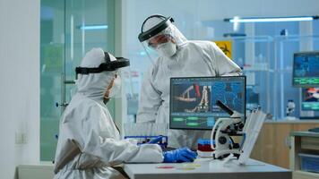 Scientist team in prorection suit arguing in front of pc looking at virus development in equipped laboratory.Team of scientists analysing vaccine evolution using high tech for researching treatment photo
