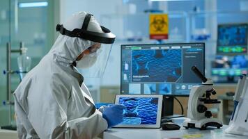 Chemists in coverall working to develop vaccine using tablet in equipped lab. Scientists examining virus evolution using high tech for scientific research of treatment development against covid19 photo