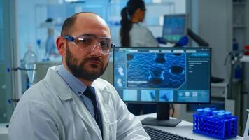 Portrait of exhausted scientist man looking at camera sitting in front of computer with DNA scan image. Chemist examining virus evolution using high tech and chemistry tools for scientific research photo