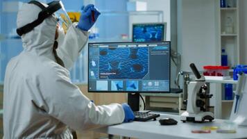 Back view of chemist man in coverall typing on computer analysing vaccine evolution in equipped laboratory. Team of doctors in ppe suit using high tech for researching treatment against covid19 virus photo