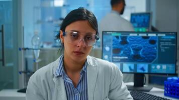 Exhausted microbiologist with protection glass sitting in laboratory looking at camera. Tired woman scientist in biotechnology laboratory wearing working hurt during global epidemic. photo