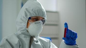 Scientist in coverall doing research analysing liquid in tube at modern equipped laboratory. Biochemist examining vaccine evolution using high tech for treatment development against covid19 virus photo