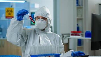 Neurologist with ppe suit working at vaccine development analysing blood sample in equipped laboratory typing on pc. Team examining virus evolution using high tech for research in treatment for covid19 photo