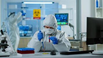 Science technician in ppe suit using micropipette and petri dish working in research laboratory analysing blood sample. Team examining virus evolution for vaccine development against covid19 photo