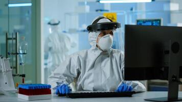 Laboratory technician assistant in ppe suit analyzing blood sample in test tube typing at pc. Doctor working with various bacteria, tissue, pharmaceutical research for antibiotics against covid19. photo
