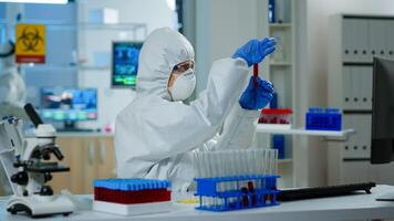 Researcher in coverall holding test tubes with blood sample for new treatment in medical laboratory. Team of doctors examining virus evolution using high tech for vaccine development against covid19 photo