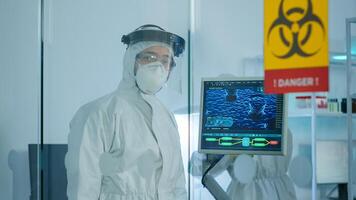 Tired doctor in protection suit against covid-19 looking exhausted at camera behind the glass wall working in danger area. Scientist examining virus evolution using high tech for scientific research photo