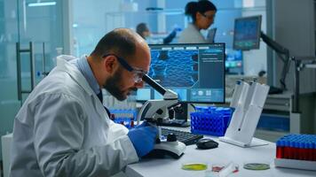 Medical research scientist conducting vaccine development under digital microscope in a biological applied science laboratory. Lab engineer working on medical treatment, typing information on computer photo