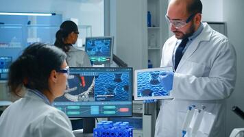 Team of industrial scientists, engineers, developers innovating new vaccine, doctor pointing on tablet explaining virus evolution to coworker. Chemist researching diagnosis in equipped laboratory. photo