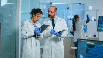 Group of medical researchers discussing about vaccine development standing in equipped lab pointing on tablet and taking notes. Doctors examining virus evolution using high tech researching diagnosis photo