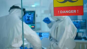 Chemists in coverall trying to develop vaccine using tablet standing behind the glass wall working in danger area of lab. Scientists examining virus evolution researching for treatment against covid19 photo