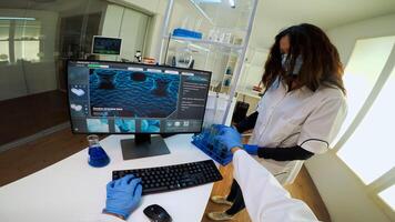 POV of researcher doctor writing at computer, analysing DNA scan image, while nurse bringing him test tube samples. Group of biochemistry scientists examining virus evolution using high tech photo
